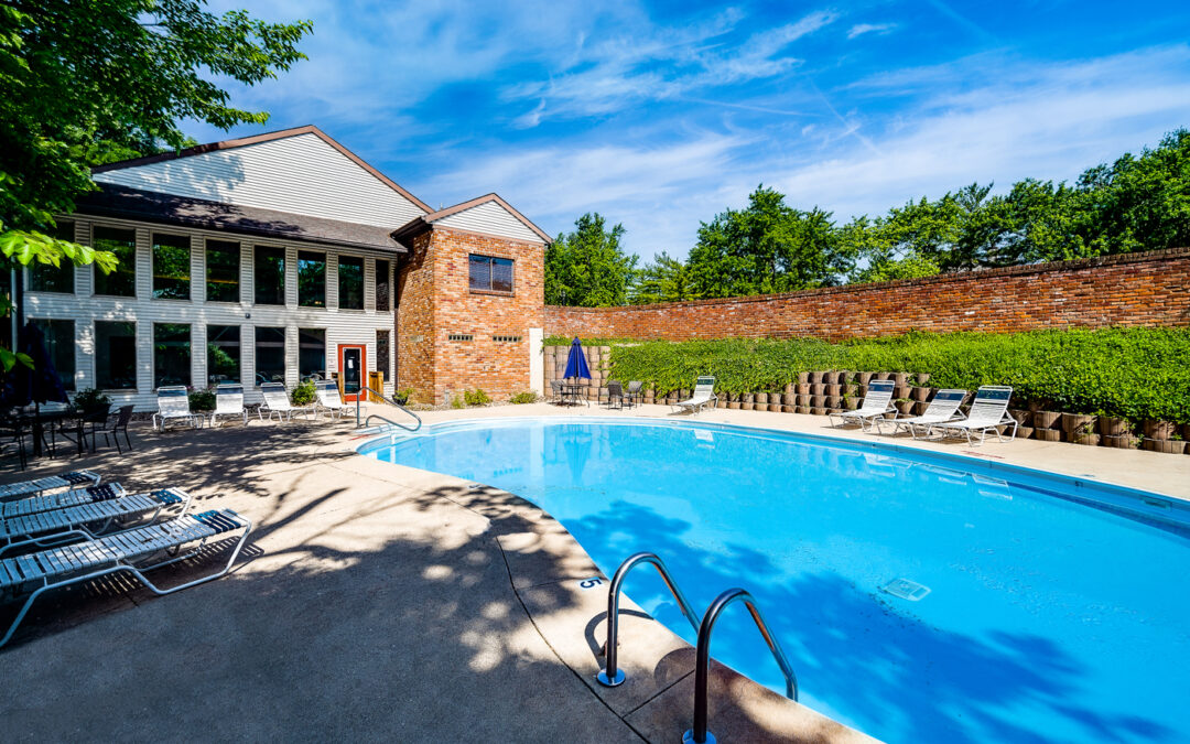 Swimming pool with chaise lounge seating, two story leasing office overlooking the pool deck, and tall brick wall on the far side with vines growing on it.