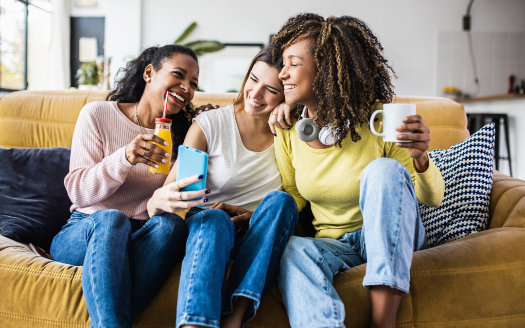 Three cheerful multiracial female friends enjoying free time together at home