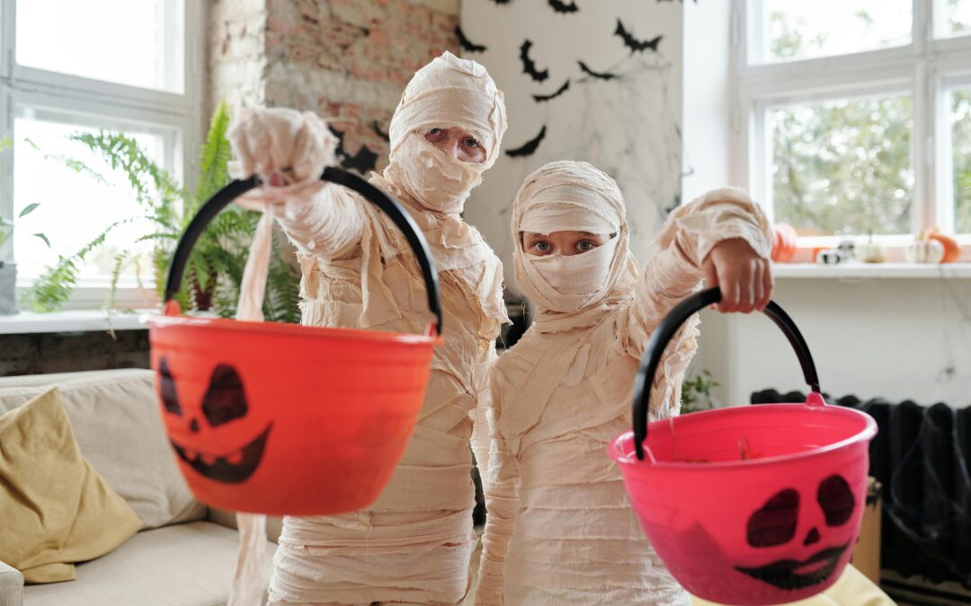 Two kids dresses as mummies hold pumpkin baskets for trick or treating