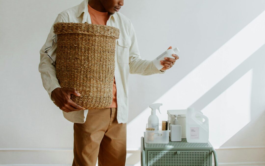 Man holding and looking at cleaning products with a trash bin in his other hand.