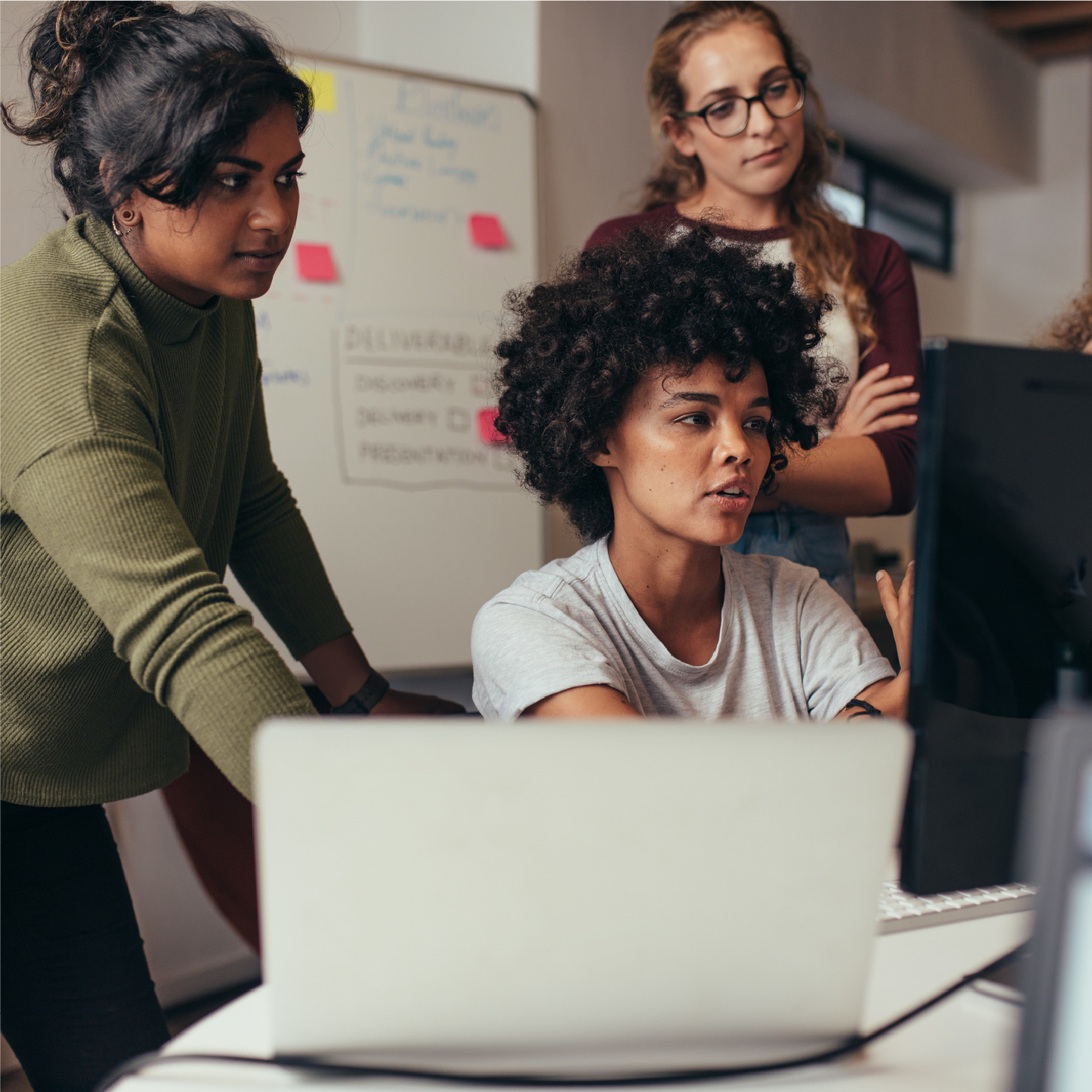 Woman sitting at desk with laptop and two women training her