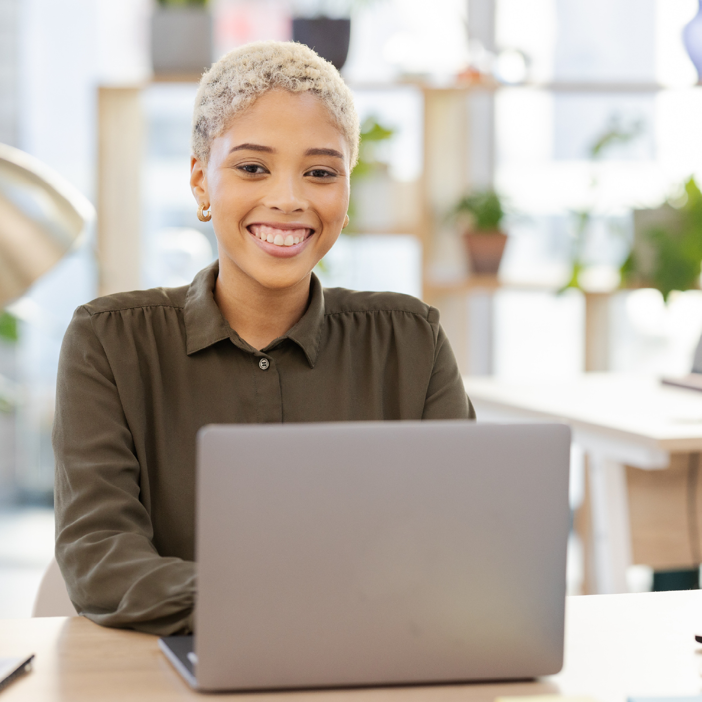 Woman sitting in office with her laptop open smiling at camera